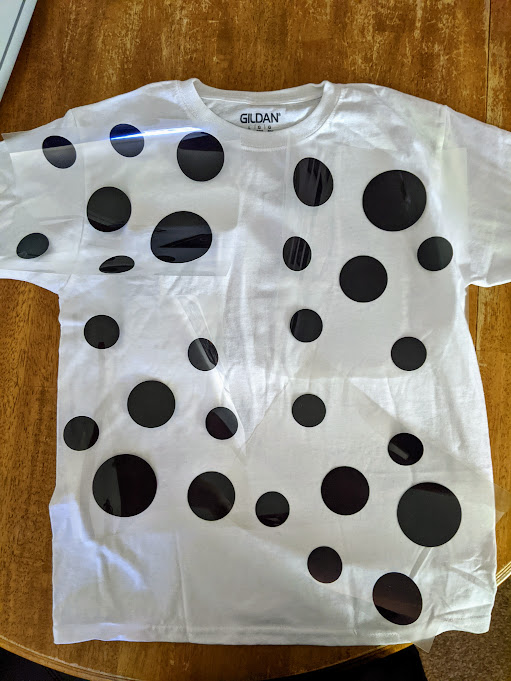 Overhead view of white tshirt laying on table with iron on spots design arranged on shirt before applying.