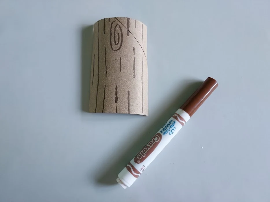 Toilet paper tube cut in half lengthwise and drawn on with brown marker to look like a log.