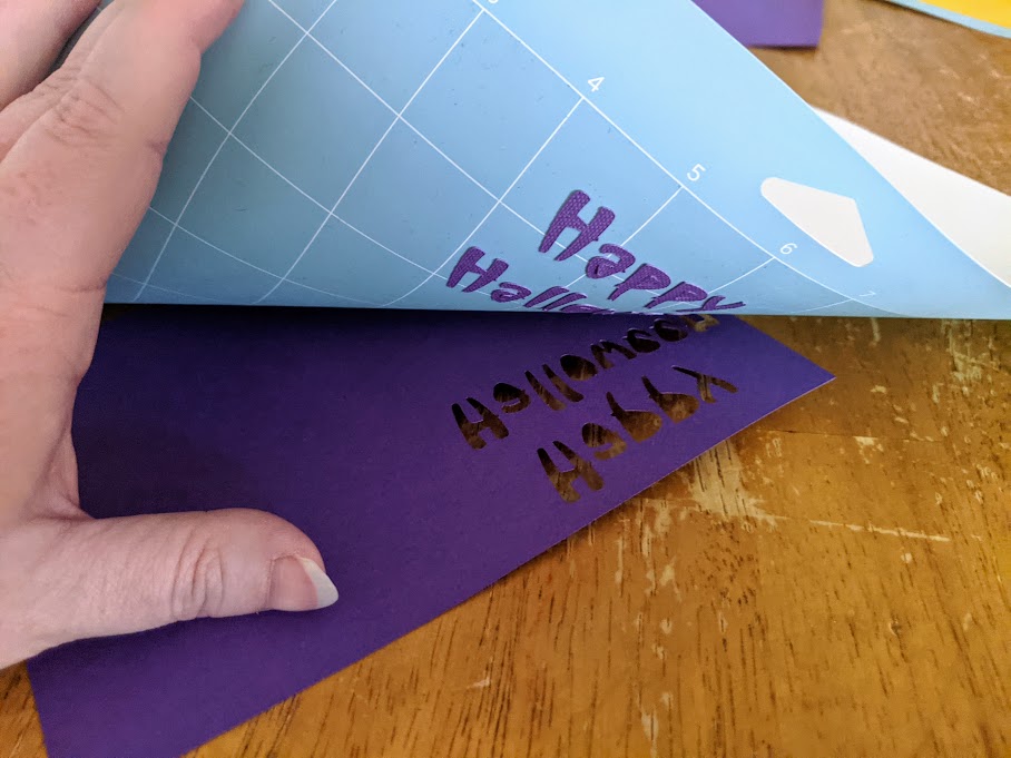 White woman's hand holding purple cardstock against table and rolling back blue machine mat.