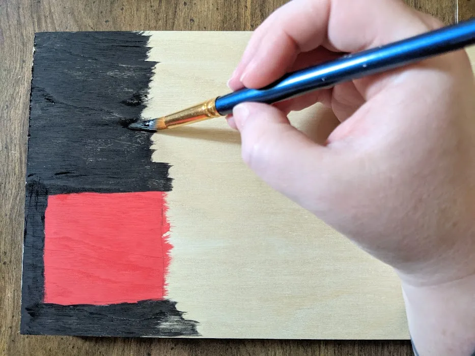 White woman's hand painting wooden sign black and red.
