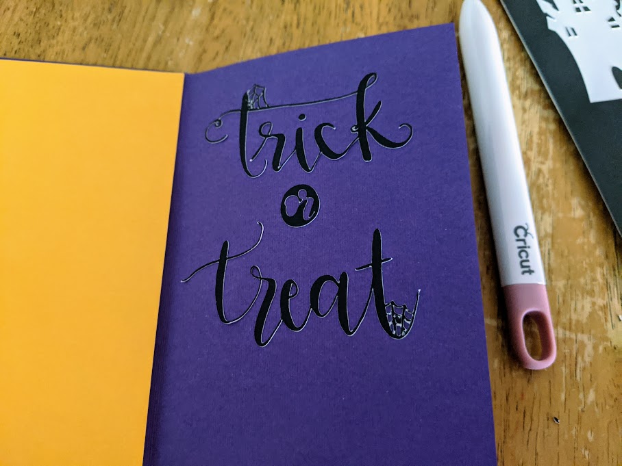 Black cardstock cut to say trick or treat with spiderwebs in some of the letters inside a purple cardstock card.