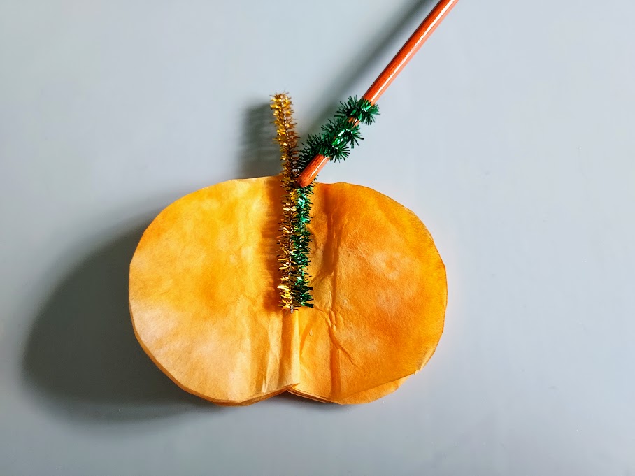 Orange and green chenille stems glued to coffee filter pumpkin with green stem wrapped around pencil to make a curly vine.
