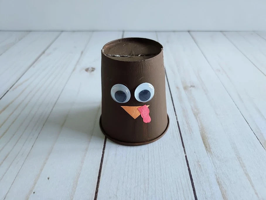 Brown painted paper cup with googly eyes, paper beak and paper snood glued to the side.