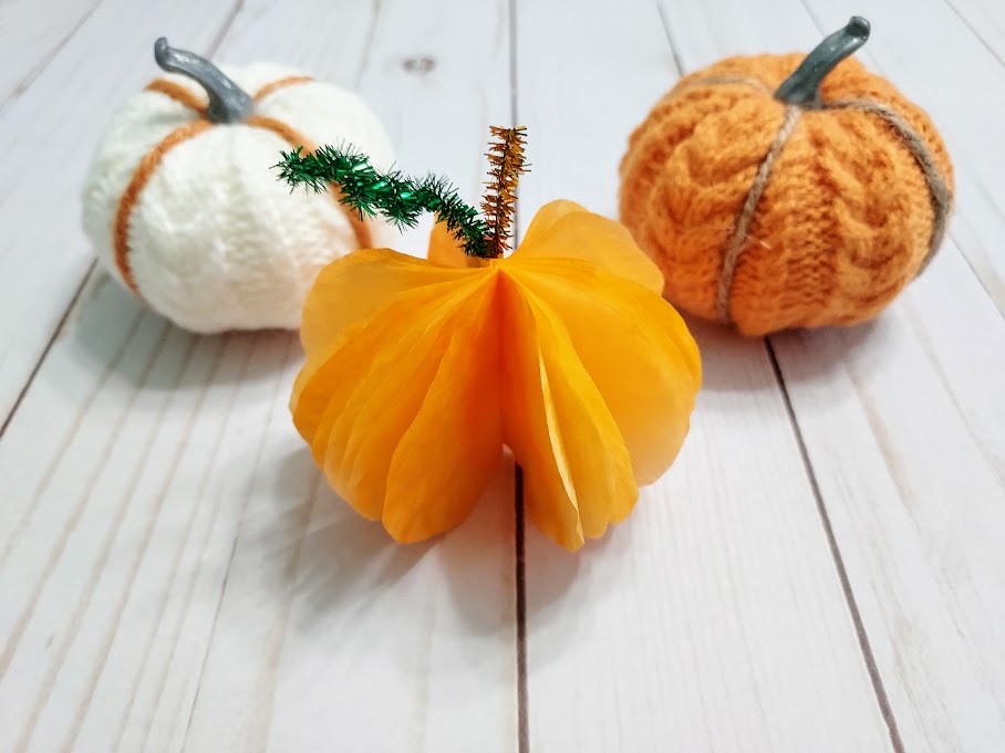 Completed 3D coffee filter pumpkin on table between two small white and orange yarn pumpkin decorations.