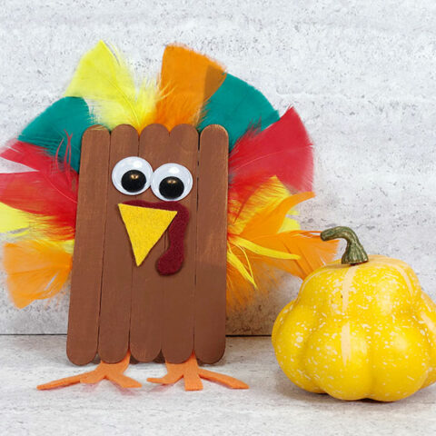 Finished popsicle stick turkey craft project next to a small yellow decorative gourd.