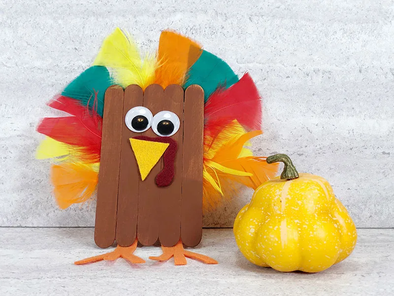 Finished popsicle stick turkey craft project next to a small yellow decorative gourd.