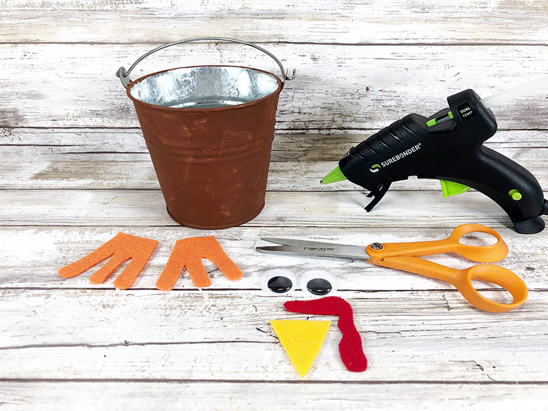 Brown painted bucket, orange felt cut like bird feet, yellow felt triangle, red felt snood, googly eyes, scissors, and hot glue gun.