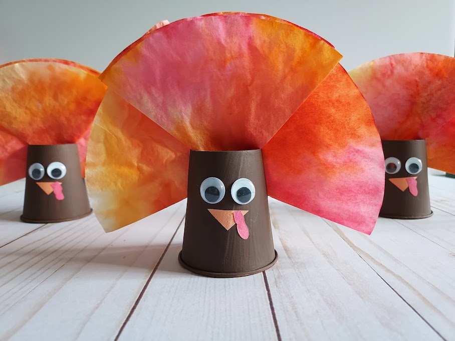 Close view of completed coffee filter paper cup turkeys. One is in the center of the photo with two others flanking behind it.