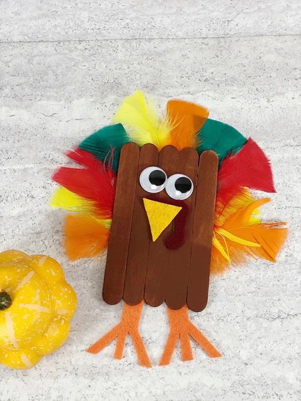 Turkey craft made with brown painted craft sticks, felt, googly eyes, and colorful feathers.