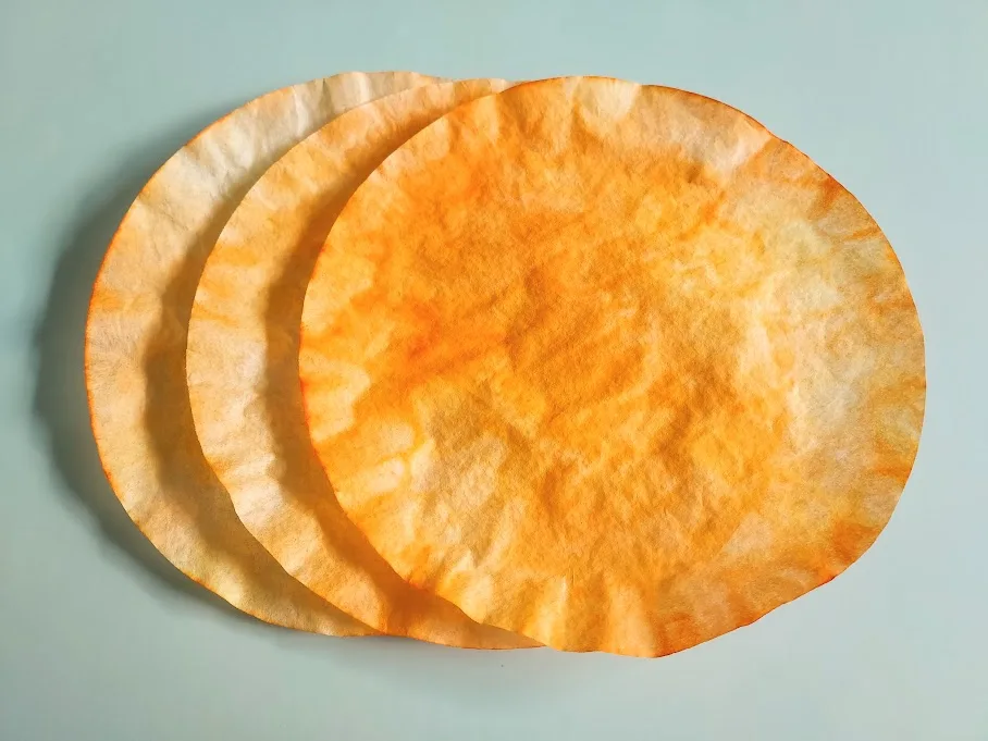 Three coffee filters colored orange and dried laying overlapping on workspace.