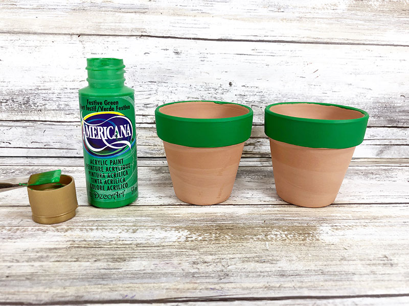 2 clay pots next to each other with the top rim outside the flower pots painted kelly green. Paint bottle sitting to the left.