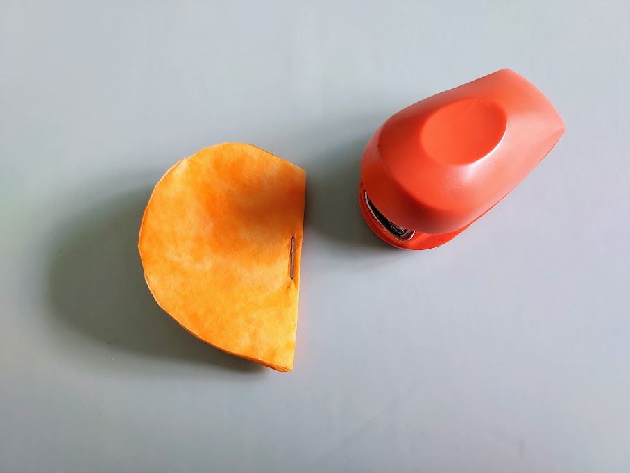 Stapling orange coffee filters together to make 3D pumpkin.