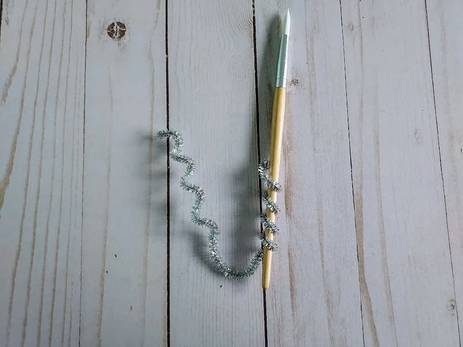 Silver chenille stem curled around pencil to make a spiral.