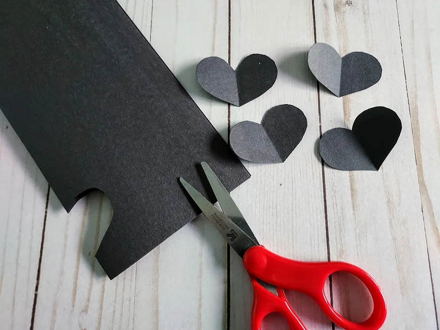 Black construction paper folded in half cutting out hearts.