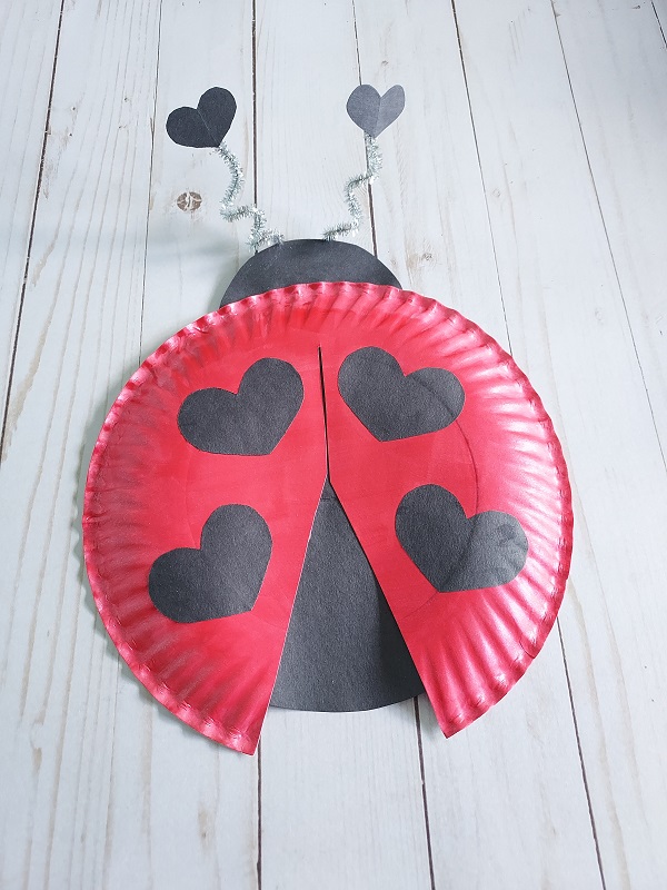 Finished love bug craft made with paper plate and construction paper. Looks like a ladybug with heart shaped spots.