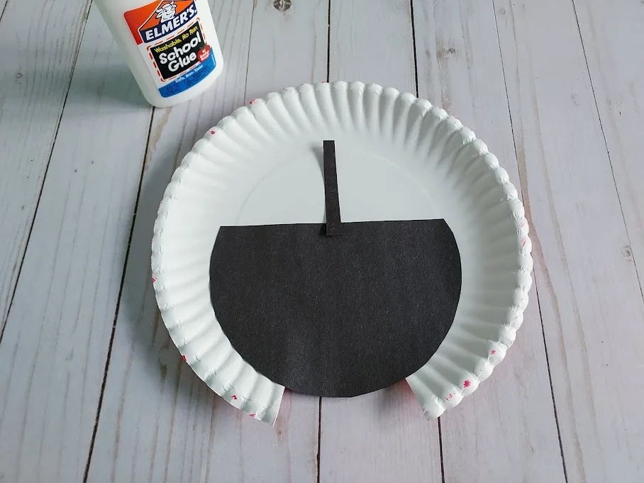 Gluing black paper body to underside of paper plate.