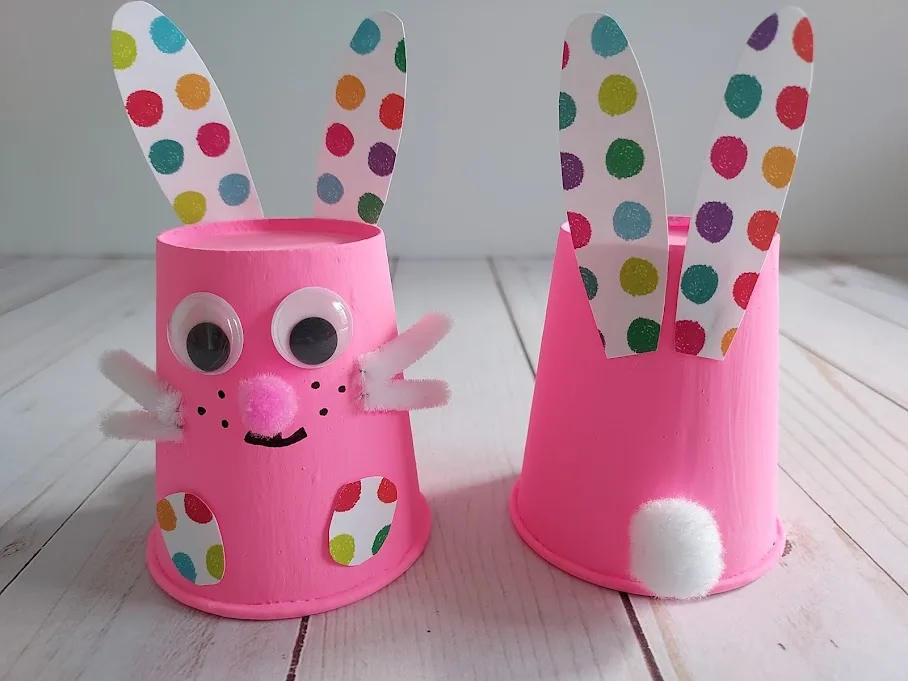 Two pink paper cup bunnies side by side. Left one is facing front and right one is turned around to see where ears and tail are glued to cup.