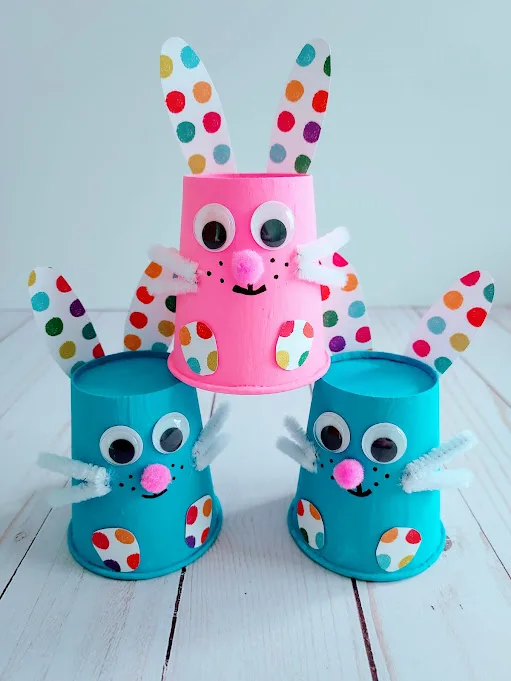 Three finished paper cup bunnies. Pink one is stacked on top of two blue ones to create a bunny pyramid.