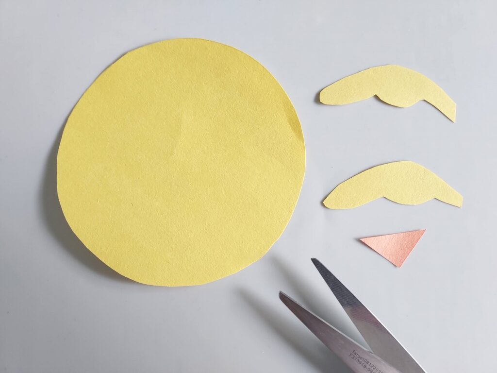 Circle and two small wing shapes cut out of yellow construction paper. Small orange triangle cut out of construction paper for chicken's beak.