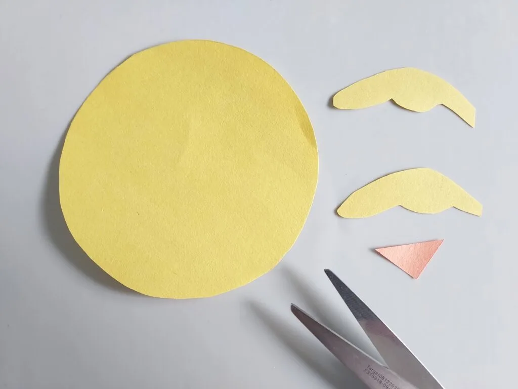 Circle and two small wing shapes cut out of yellow construction paper. Small orange triangle cut out of construction paper for chicken's beak.
