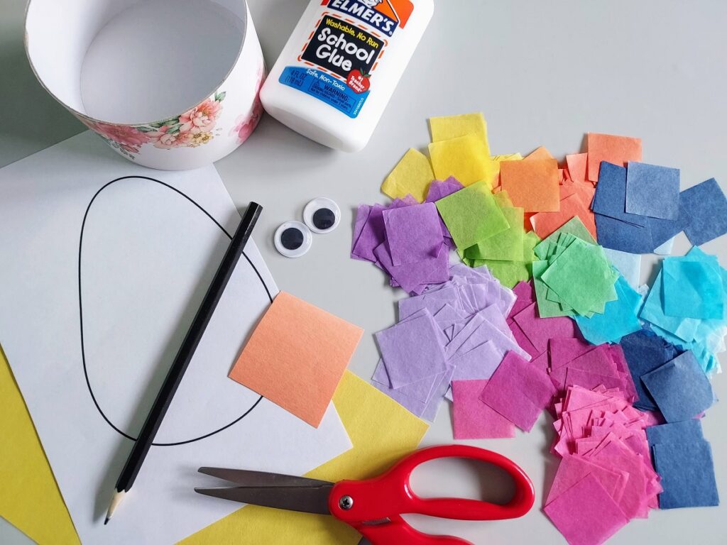 Cup, bottle of glue, Easter egg template on white paper, googly eyes, pencil, yellow and orange construction paper, red handled scissors, and an assortment of bright colored tissue paper squares on table.