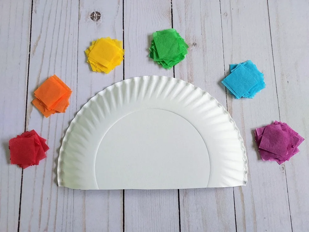 Piles of square tissue paper sorted by color and arranged in rainbow order above white paper plate cut to give a straight bottom edge.