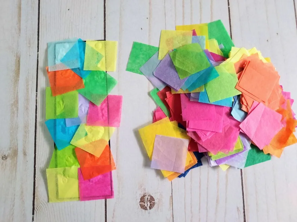 Single bookmark template completely covered with colored tissue paper laying on table next to pile of tissue paper squares.