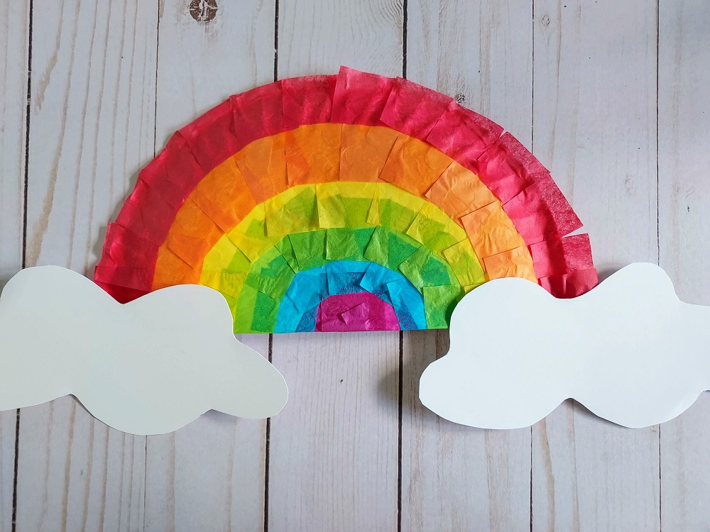 Overhead view of completed paper plate rainbow with tissue paper colors and white paper clouds.