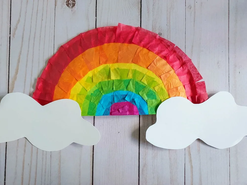Overhead view of completed paper plate rainbow with tissue paper colors and white paper clouds.