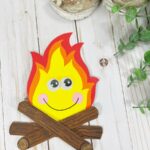 Overhead view of a completed campfire craft made with popsicle sticks and colored cardstock. The fire also has a kawaii face.