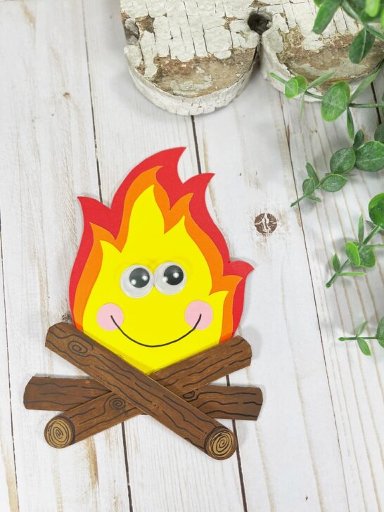 Overhead view of a completed campfire craft made with popsicle sticks and colored cardstock. The fire also has a kawaii face.