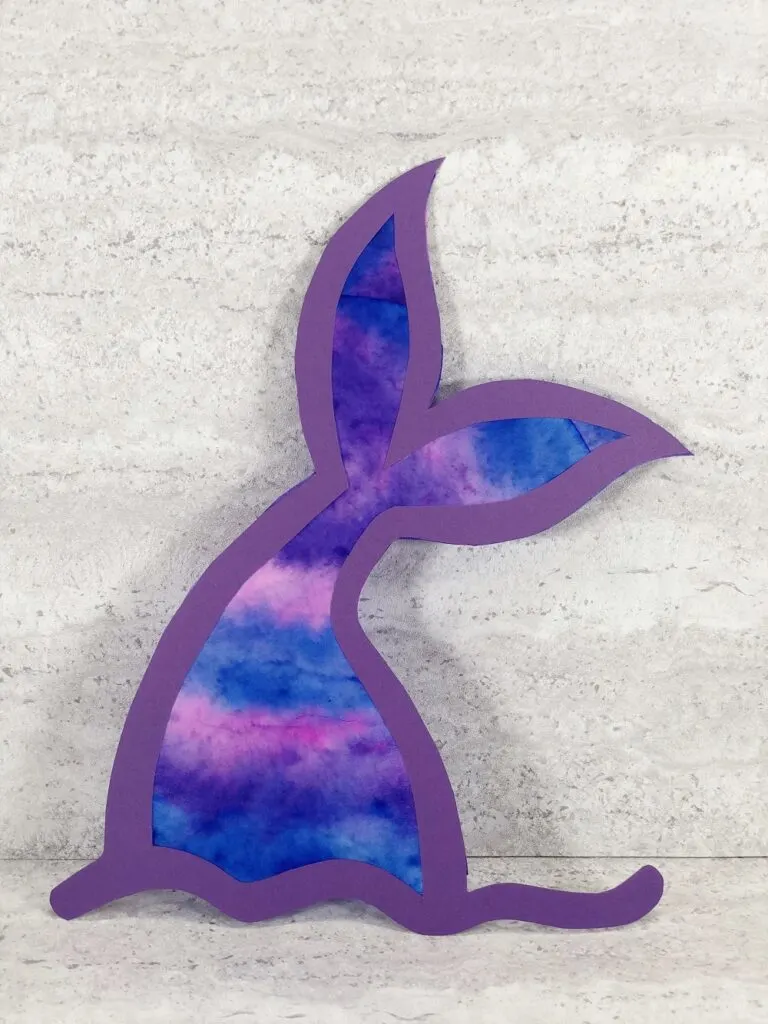 Completed coffee filter mermaid tail suncatcher made with a bright and colorful coffee filter inside a purple cardstock outline.