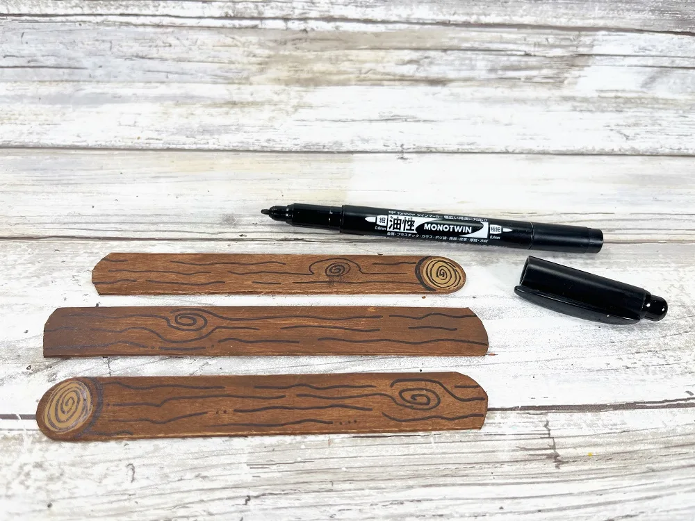 Black marker used to draw lines and swirls on the three brown painted popsicle craft sticks to make them look like logs.