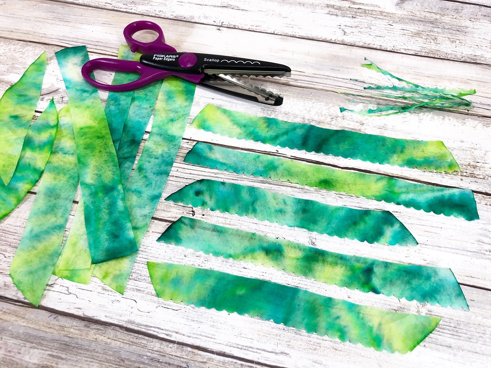 Strips of green colored coffee filter cut with a scallop scissors giving one edge a wavy look.