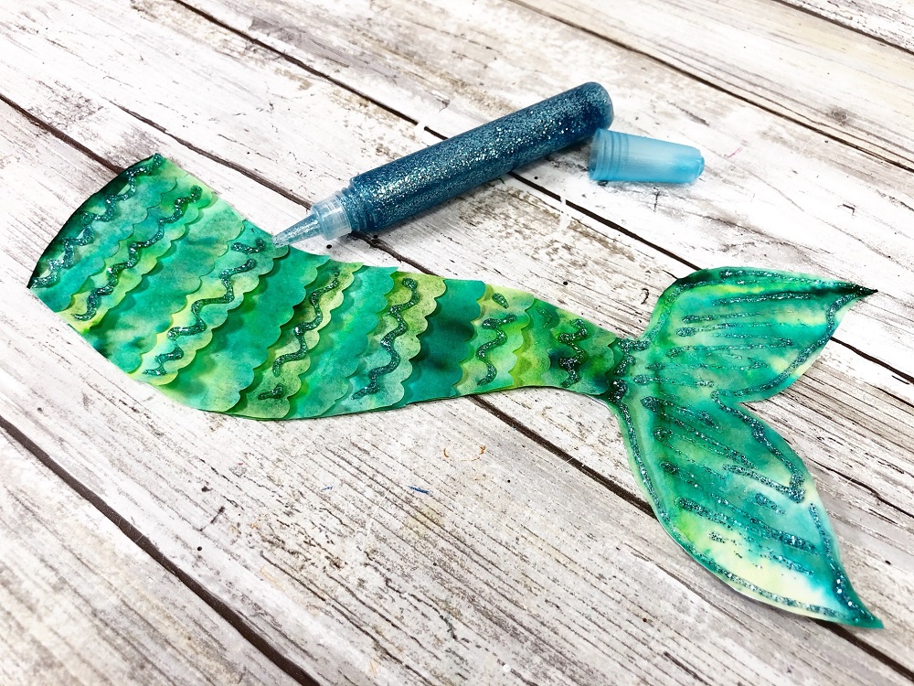 Green tie dyed coffee filter mermaid tail decorated with green glitter glue pen.