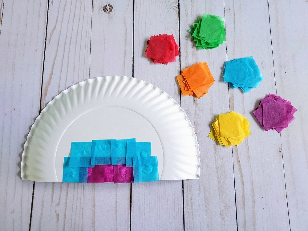 Purple and light blue tissue paper glued to white paper plate. Tissue paper pieces sorted by rainbow color arranged next to plate.