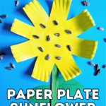 Overhead view of completed craft for kids making a sunflower out of a paper plate and popsicle stick. Yellow paper plate sunflower is laying on blue background with sunflower seeds scattered around it. White text with black outline near bottom says Paper Plate Sunflower.