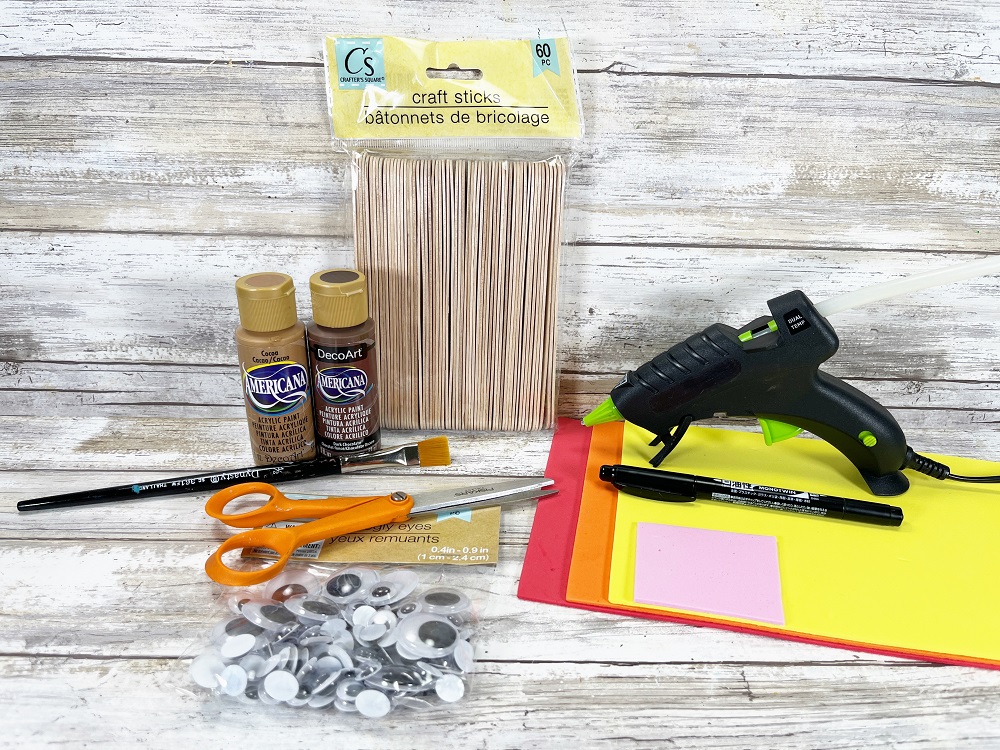 Supplies needed for creating this campfire craft. Includes jumbo popsicle sticks, googly eyes, scissors, paint brush, brown paint, tan paint, red paper, orange paper, yellow paper, pink paper, black marker, and hot glue gun.
