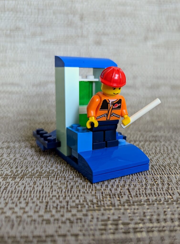 Close up view of small LEGO creation made with blue bricks to look like a little dock with a doorway. A minifig holding a white pole positioned like he is fishing.