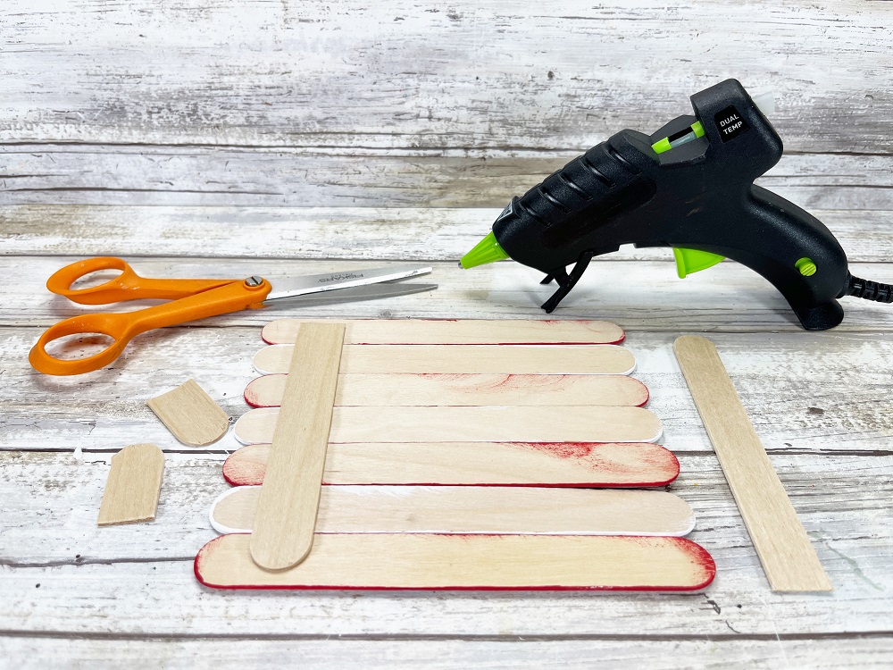 Scissors and hot glue gun sitting behind popsicle sticks arranged together with one glued along the back to hold them together.