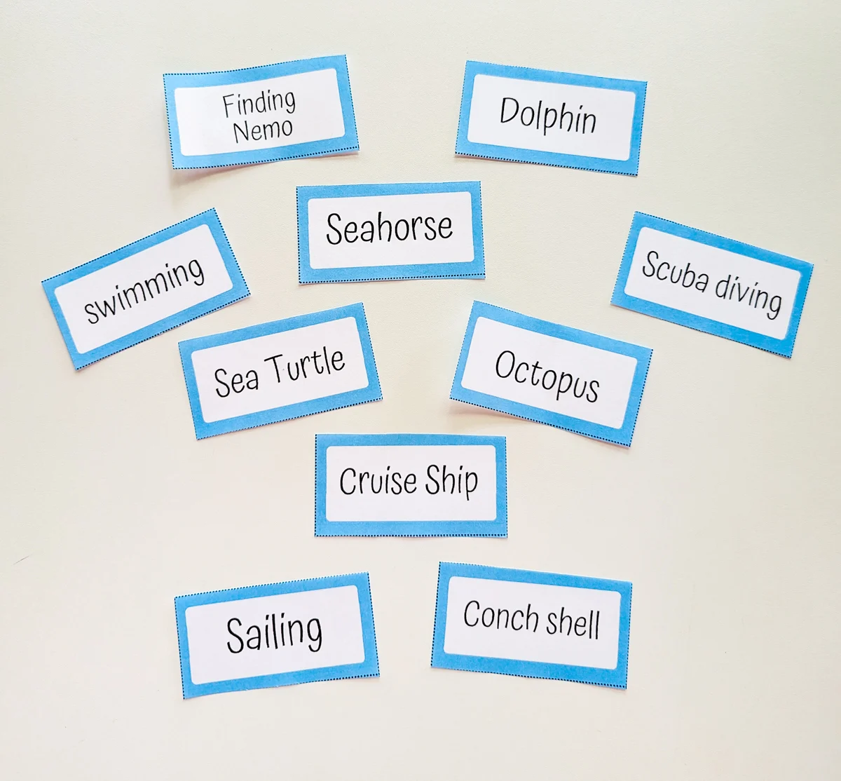 Ten word cards individually cut out from ocean charades game and spread out on white table.