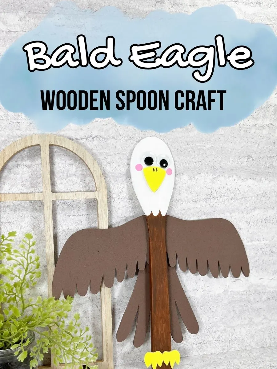 White and black text on a blue watercolor splash near the top says Bald Eagle Wooden Spoon Craft. A Bald Eagle made using a wooden cooking spoon, paint, and craft foam is completely assembled and leaning against the wall.
