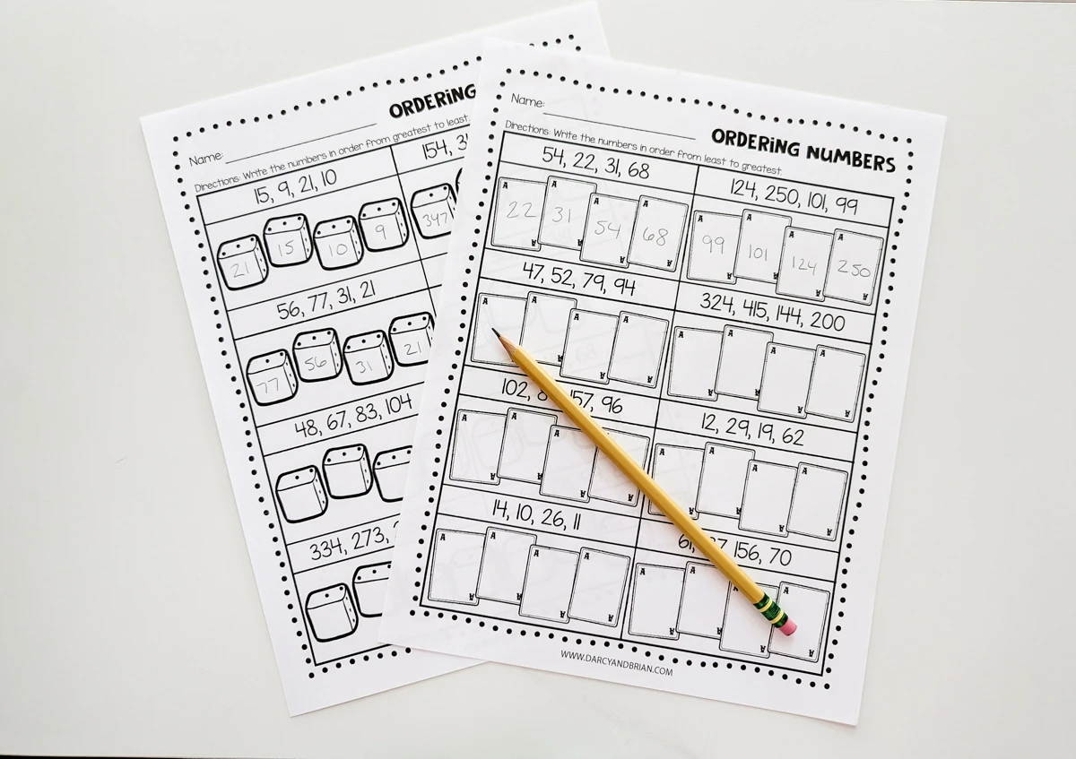 Two printed out worksheets showing some of the number order answers filled in. A pencil is laying diagonally across the paper.