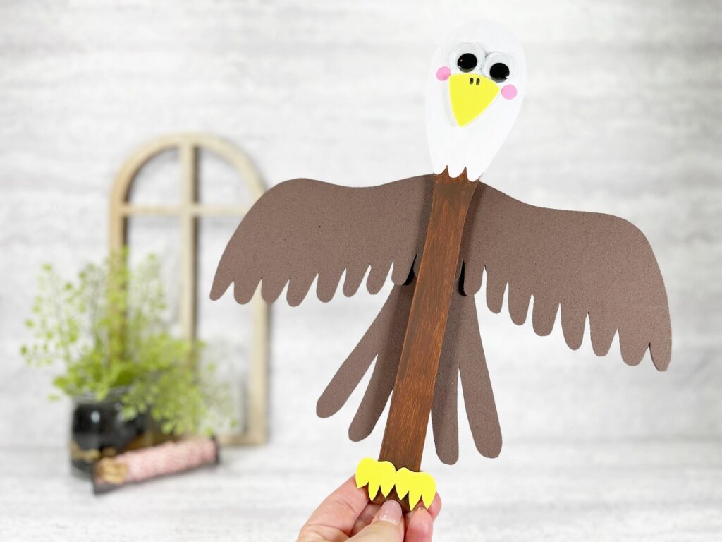 Caucasian woman's hand holding finished wooden spoon Bald Eagle craft at an angle with head tipped towards the upper right.