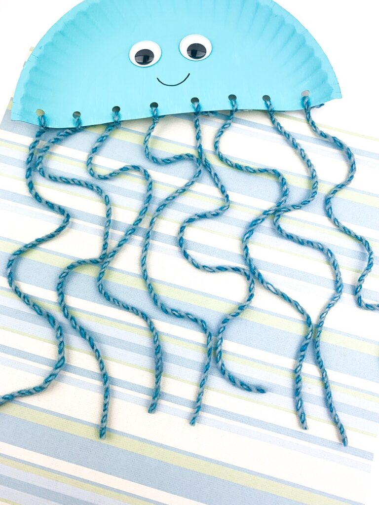 Jellyfish made using a blue painted paper plate cut in half and blue yarn hanging down.