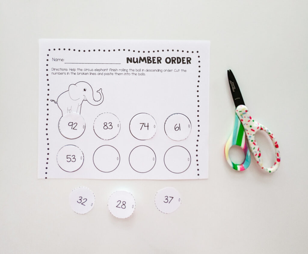 Number order worksheet with a circus elephant on it. Circus balls cut out and arranged in order. Pair of colorful kids scissors lay to the right of the paper.