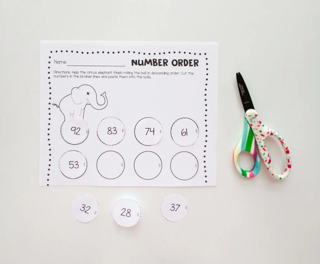 Number order worksheet with a circus elephant on it. Circus balls cut out and arranged in order. Pair of colorful kids scissors lay to the right of the paper.