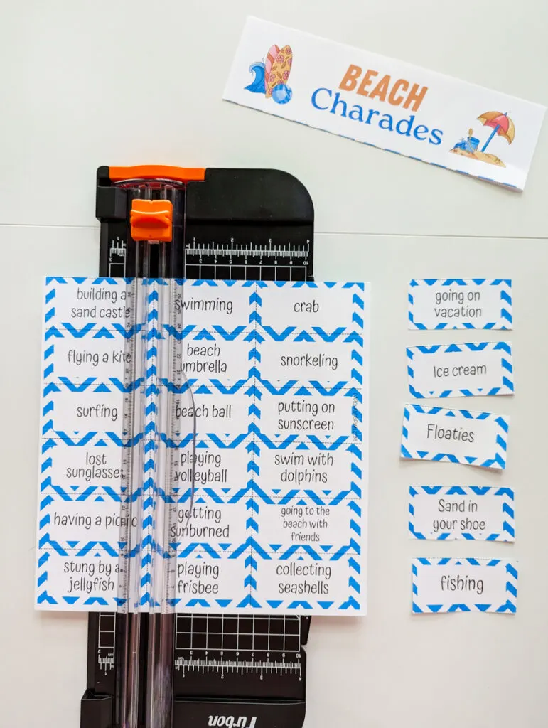 Sheet of beach charade words in a small black paper cutter. About 5 word cards cut out are lined up along the right hand side.