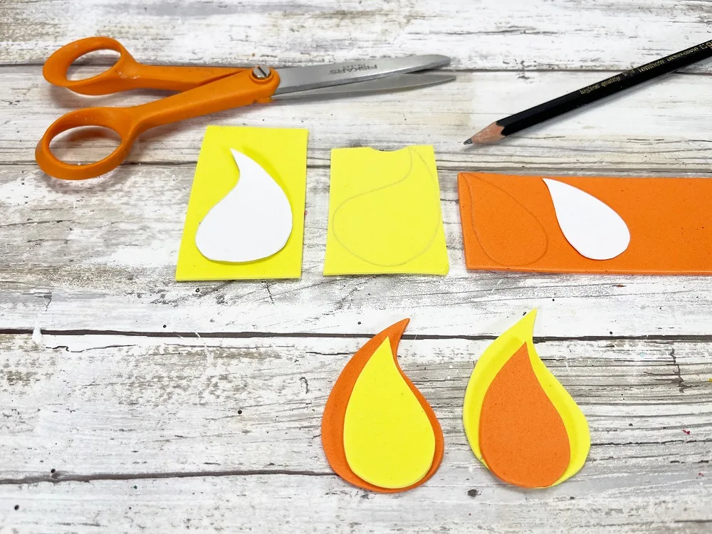 Candle flame shapes being cut out of yellow and orange craft foam.
