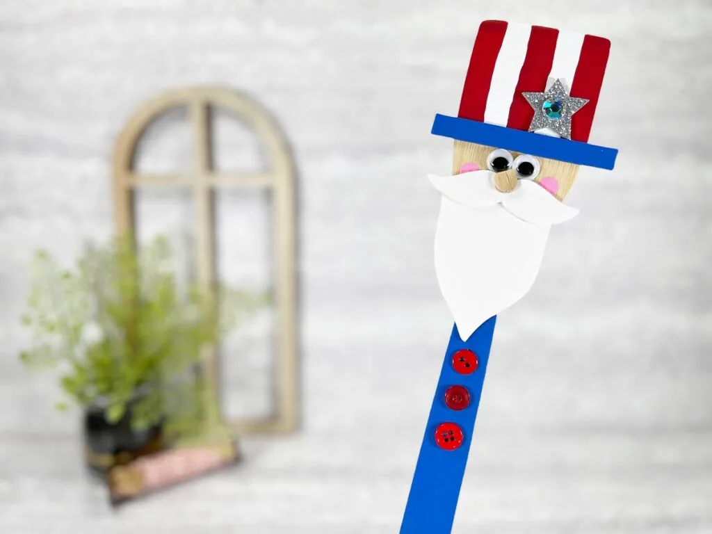 Completed Uncle Sam craft made by painting a wood spatula is held up at an angle, tilted towards the right side of the photo.